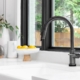 Kitchen sink detail shot in a modern, renovated kitchen with black window frames, a dark faucet, white cabinets, farmhouse sink, and cozy decor