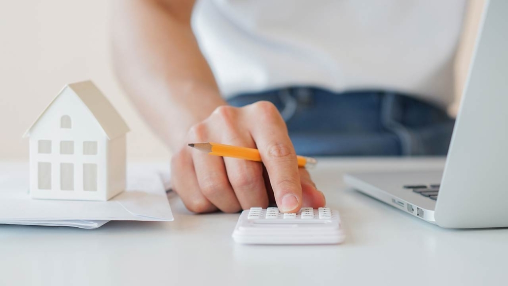 Close up of a mans hand with a pencil calculating with a small home model