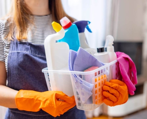 woman in rubber gloves with basket of cleaning supplies ready to clean up her apartment